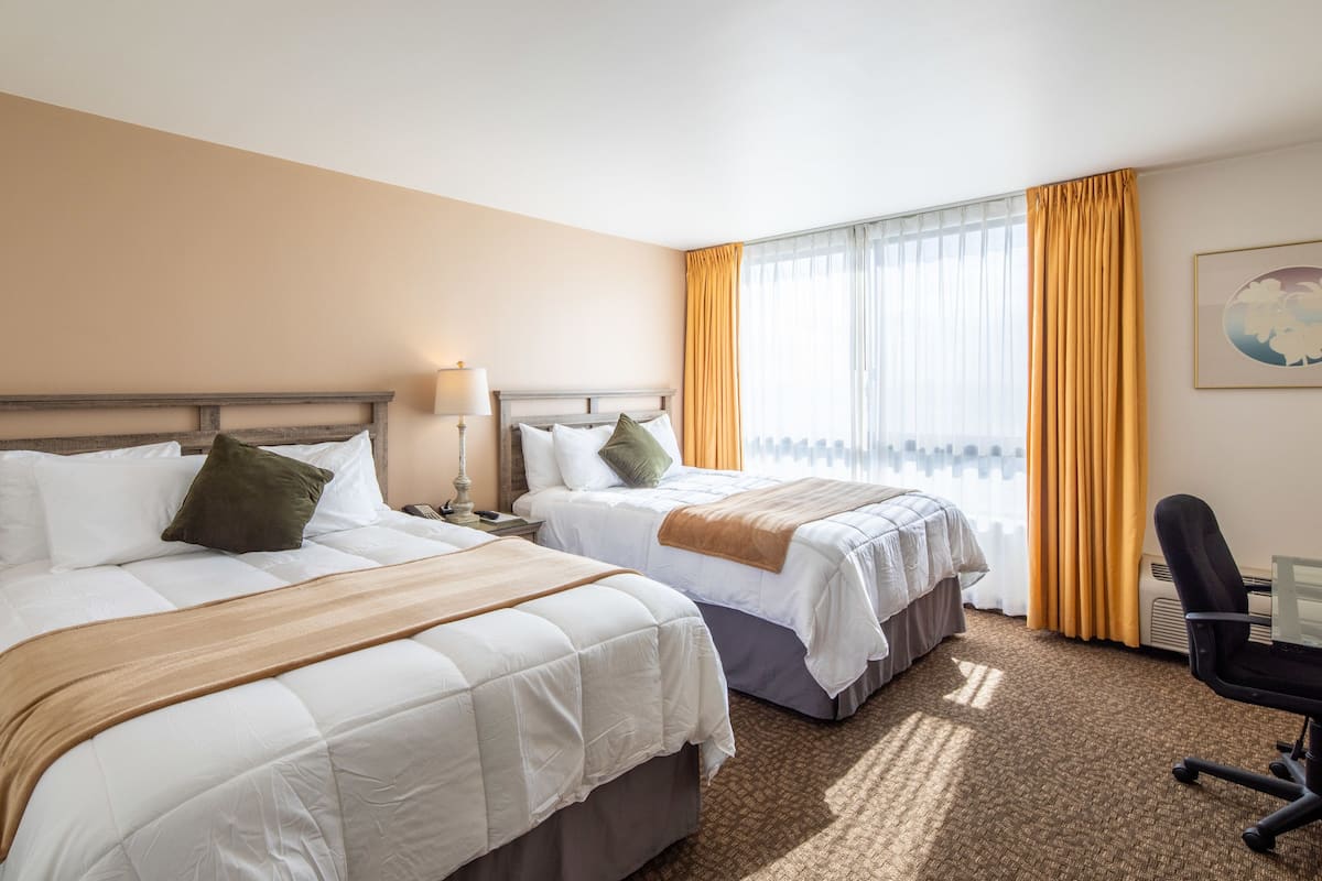 A hotel room with two beds, a desk, and a chair.
