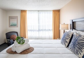 A hotel room with a bed, a chair, a lamp, and a window with curtains.