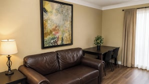 A brown leather sofa, a dining table with chairs, a potted plant, and a painting on the wall. - Plantation Oaks Suites & Inn Millington (Millington)