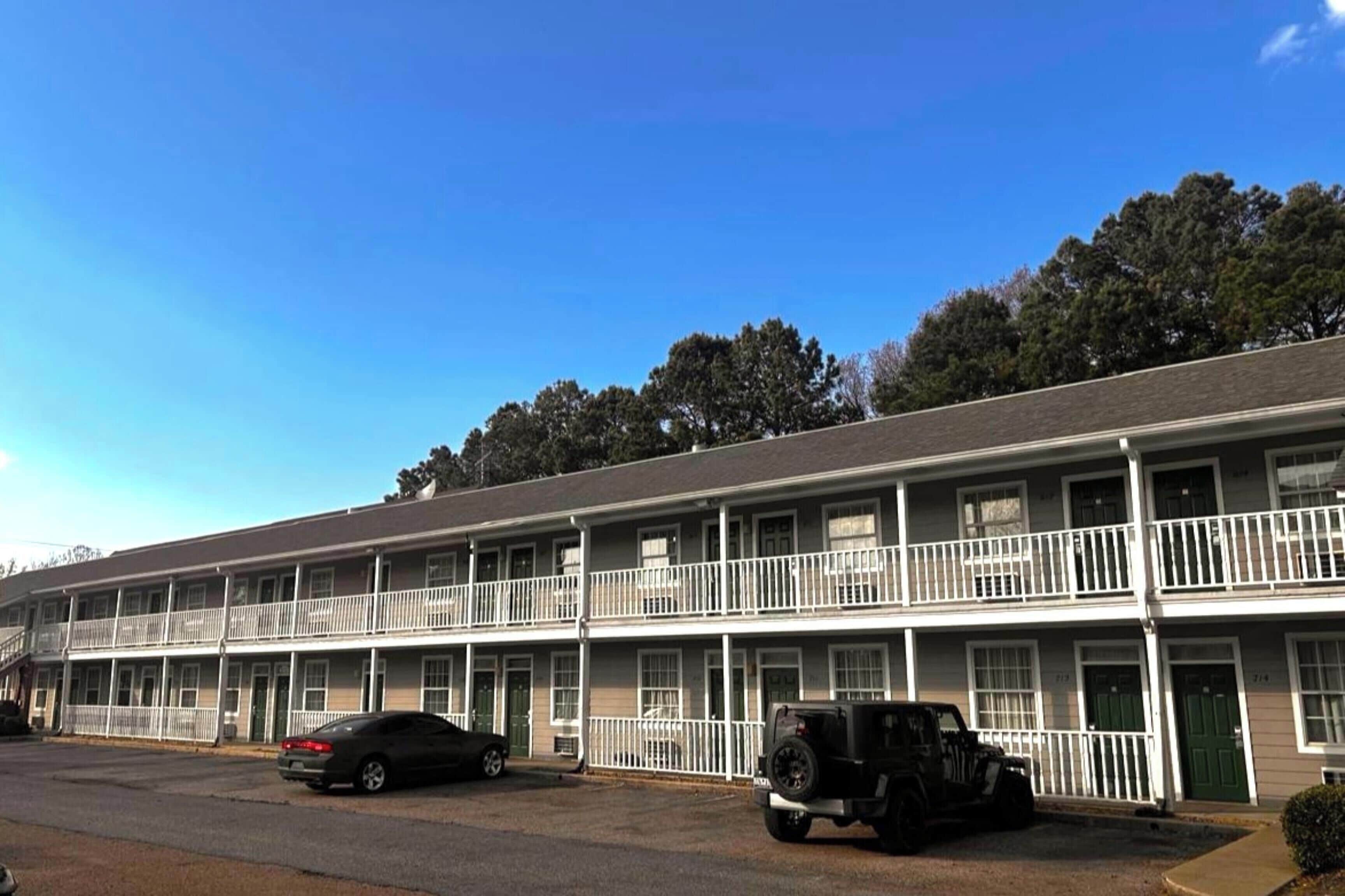 A multi-story motel with a central corridor, individual rooms on either side, and a parking lot with cars.