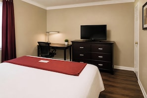 A hotel room with a bed, a desk with a chair, a television, and a dresser.