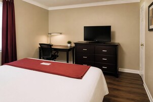 Una habitación de hotel con cama, un escritorio con silla, televisor y cómoda.