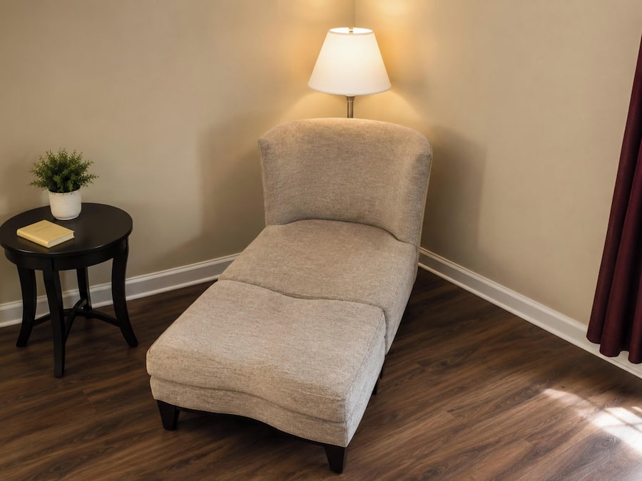 A single-occupancy room with a cushioned bench, a small table with a plant, and a lamp.