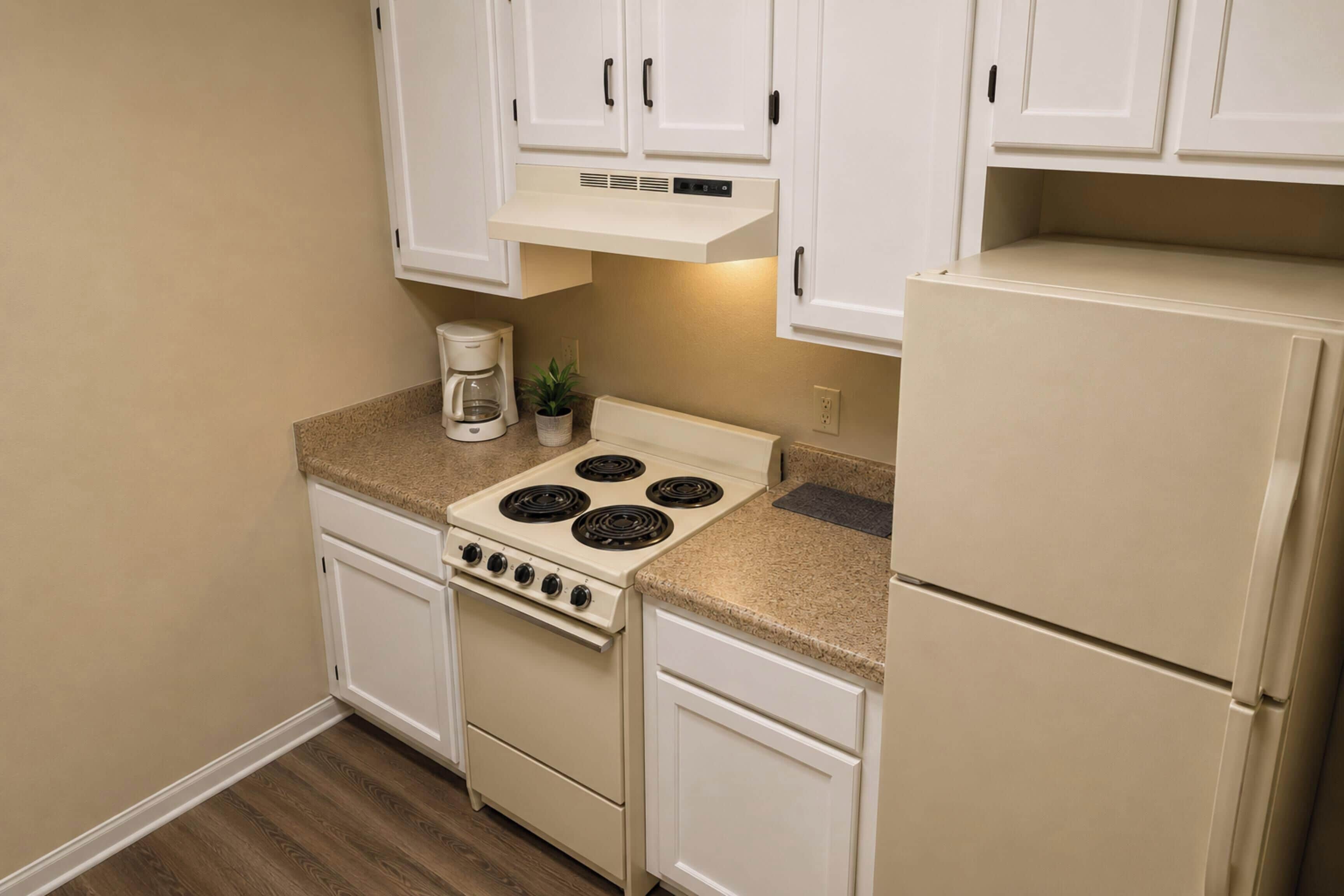 A compact kitchen with white cabinets, a stove, a coffee maker, and a refrigerator.