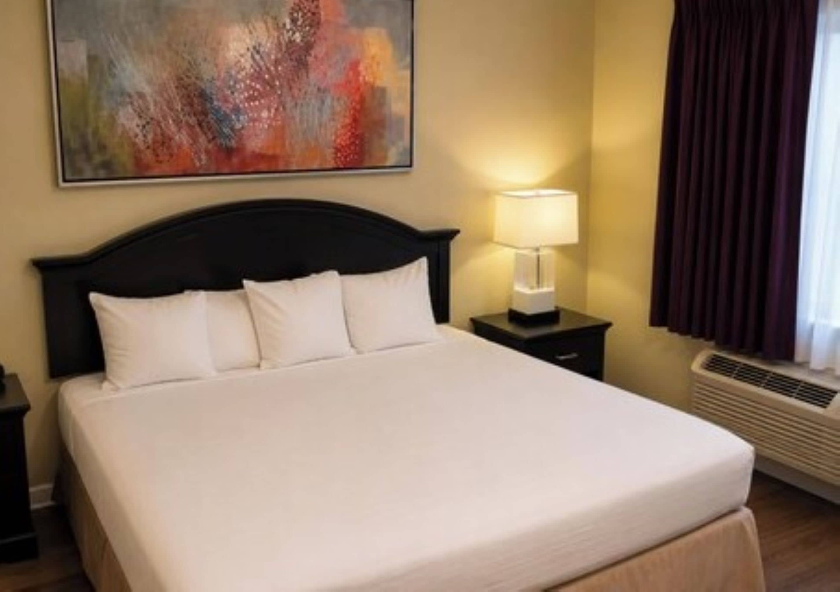 A hotel room with a large bed, a nightstand with a lamp, and a painting on the wall.