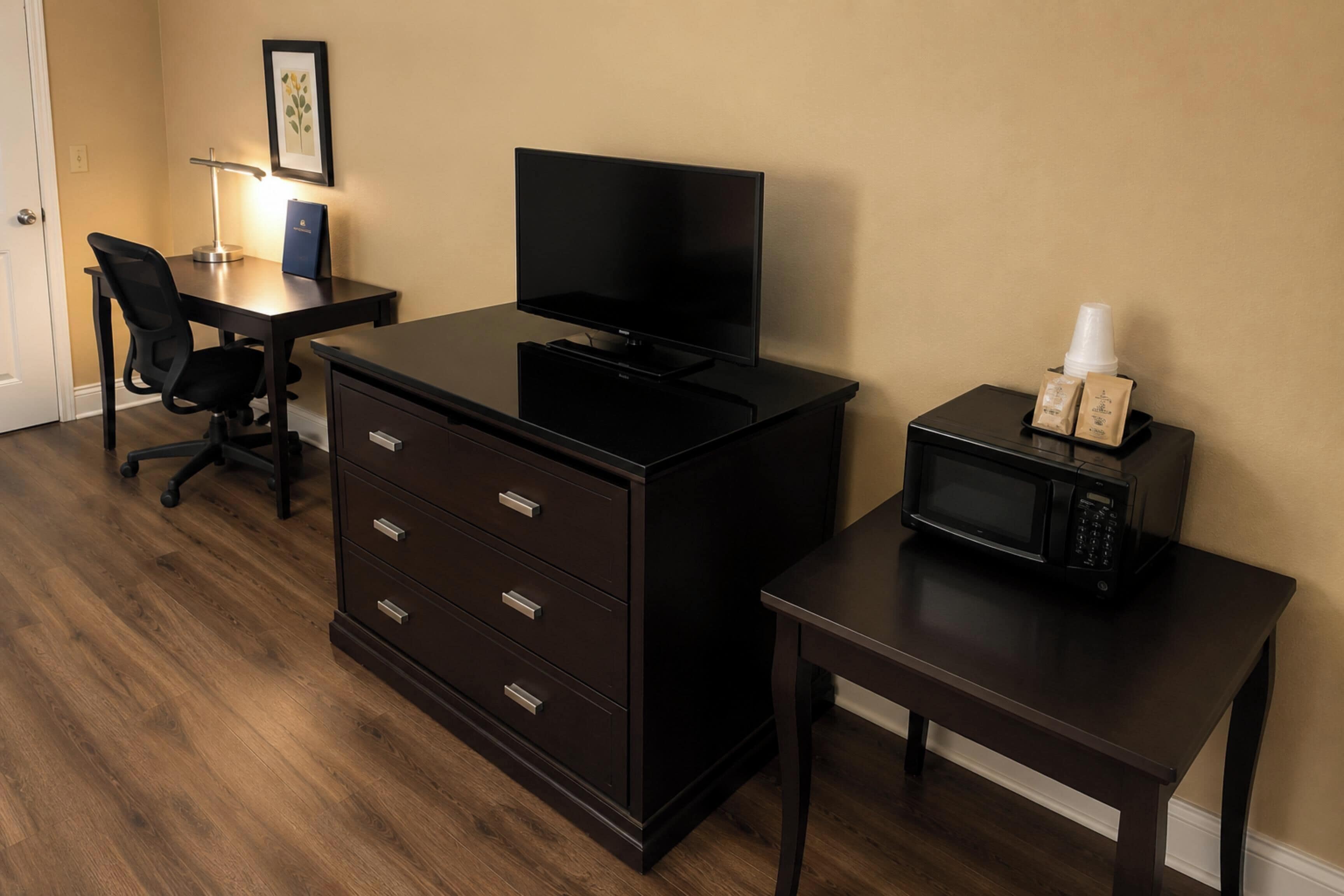 A hotel room with a desk, a television, a dresser, a microwave, and a chair.