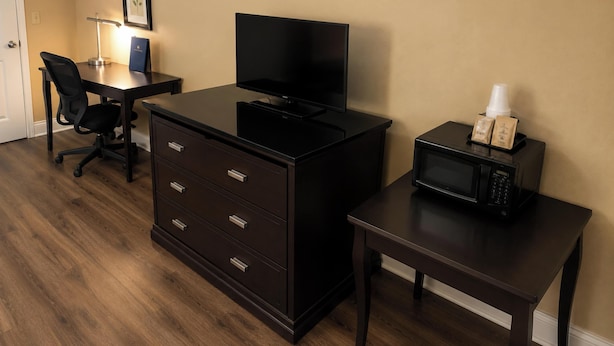 A hotel room with a desk, a television, a dresser, a microwave, and a chair. - Plantation Oaks Suites & Inn Millington (Millington)