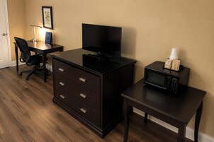 Una habitación de hotel con escritorio, televisor, cómoda, microondas y una silla.