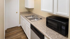A compact kitchen with a double sink, a dishwasher, and a black microwave. - Plantation Oaks Suites & Inn Millington (Millington)