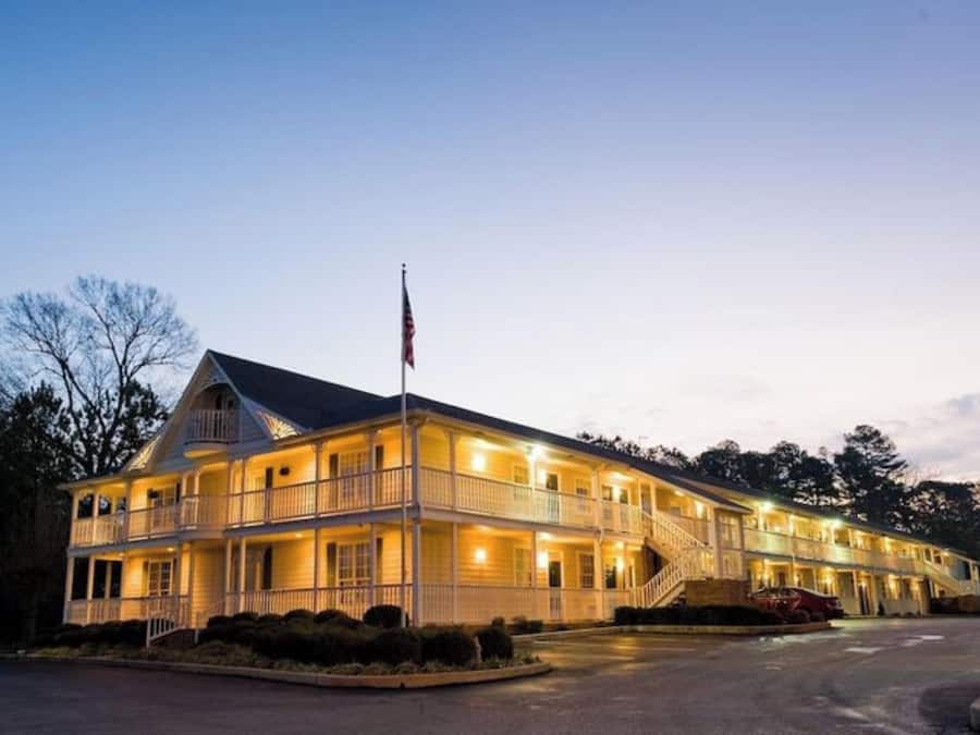 A two-story hotel with a balcony on the second floor, a flagpole with an American flag, and a parking lot in front.