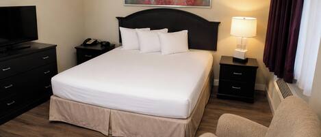 A hotel room with a bed, a desk, a chair, a television, and a painting on the wall.