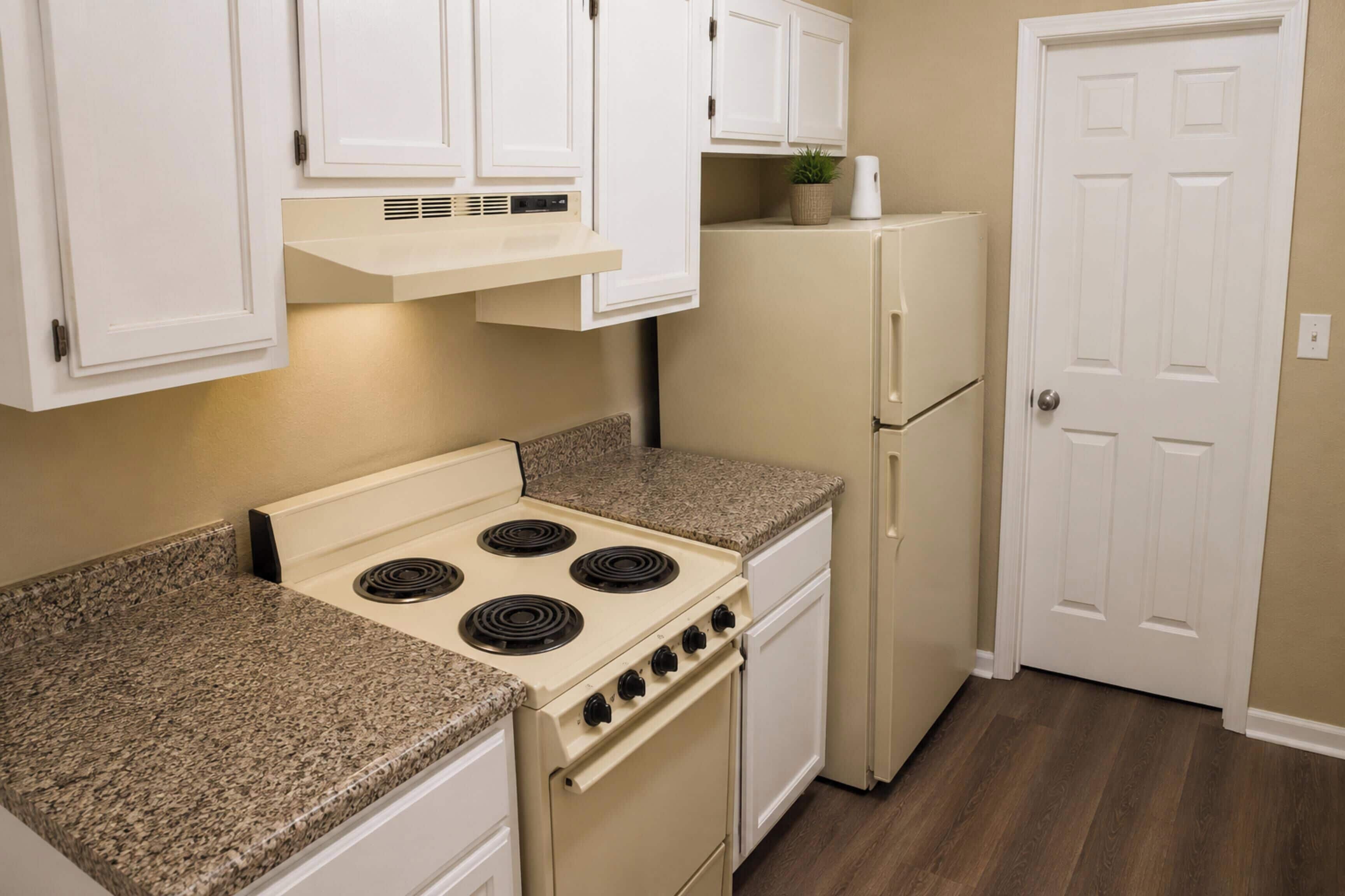 Una cocina con armarios blancos, estufa, refrigerador y una puerta.