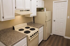 A kitchen with white cabinets, a stove, a refrigerator, and a door.