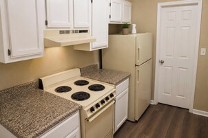 A kitchen with white cabinets, a stove, a refrigerator, and a door.