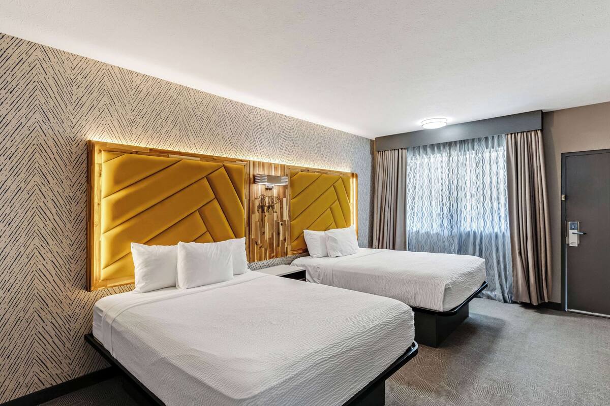 Une chambre d’hôtel avec deux lits, une grande tête de lit et un mur décoré d’un motif.