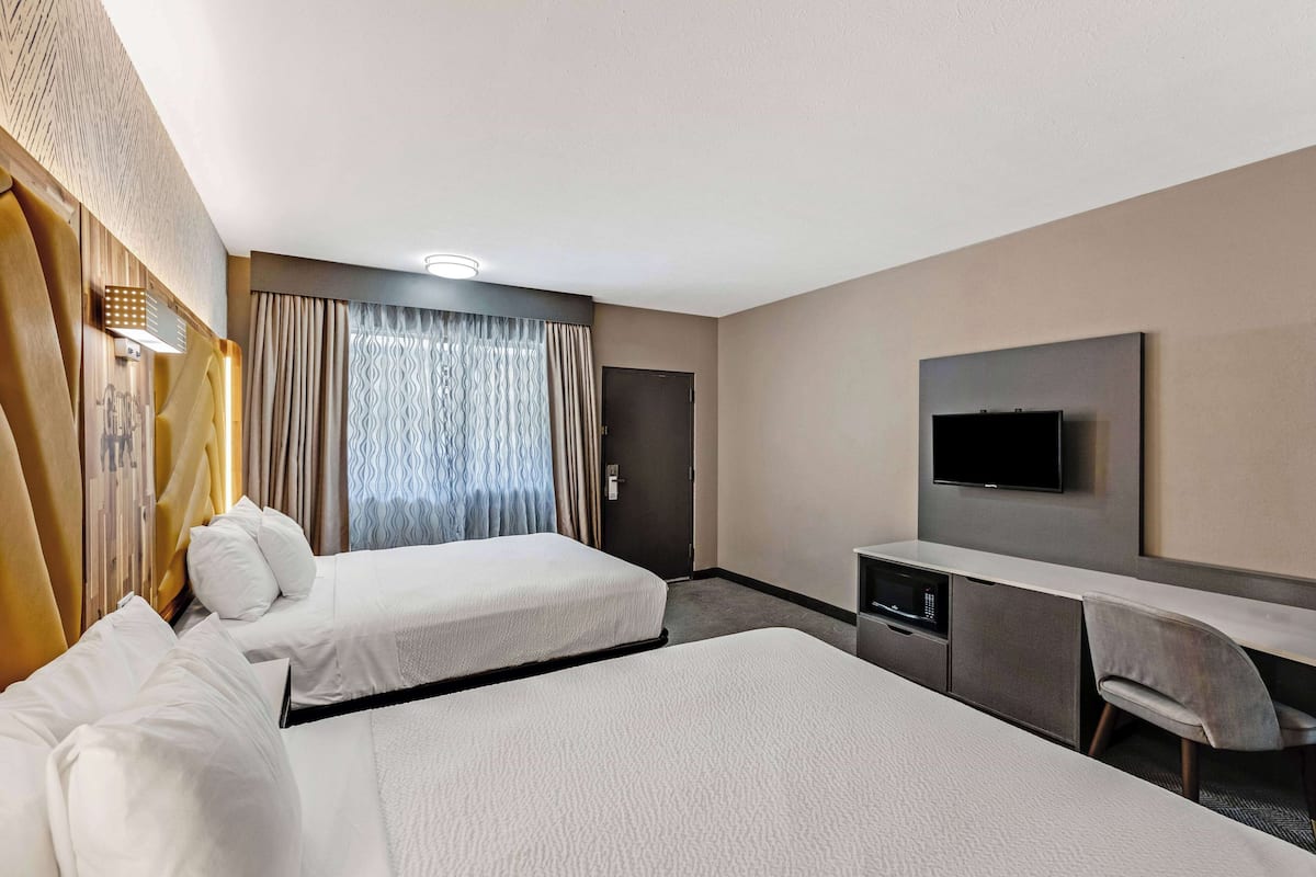 Une chambre d’hôtel avec deux lits, un bureau, une télévision et une porte.