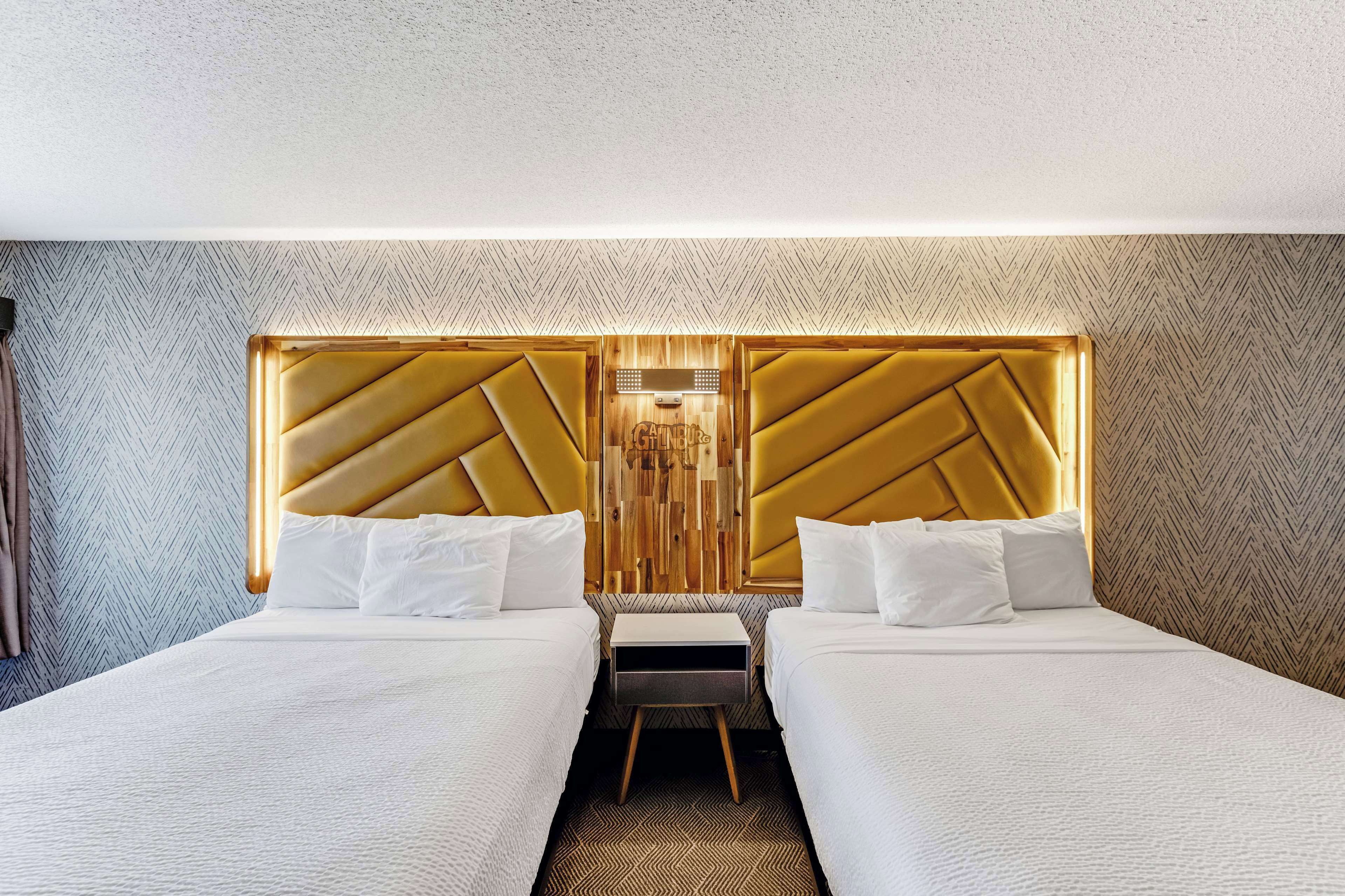 A hotel room with two beds, a wooden headboard, and a small bedside table.