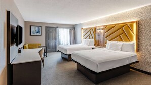 A hotel room with two beds, a desk, a TV, and a large window with curtains.