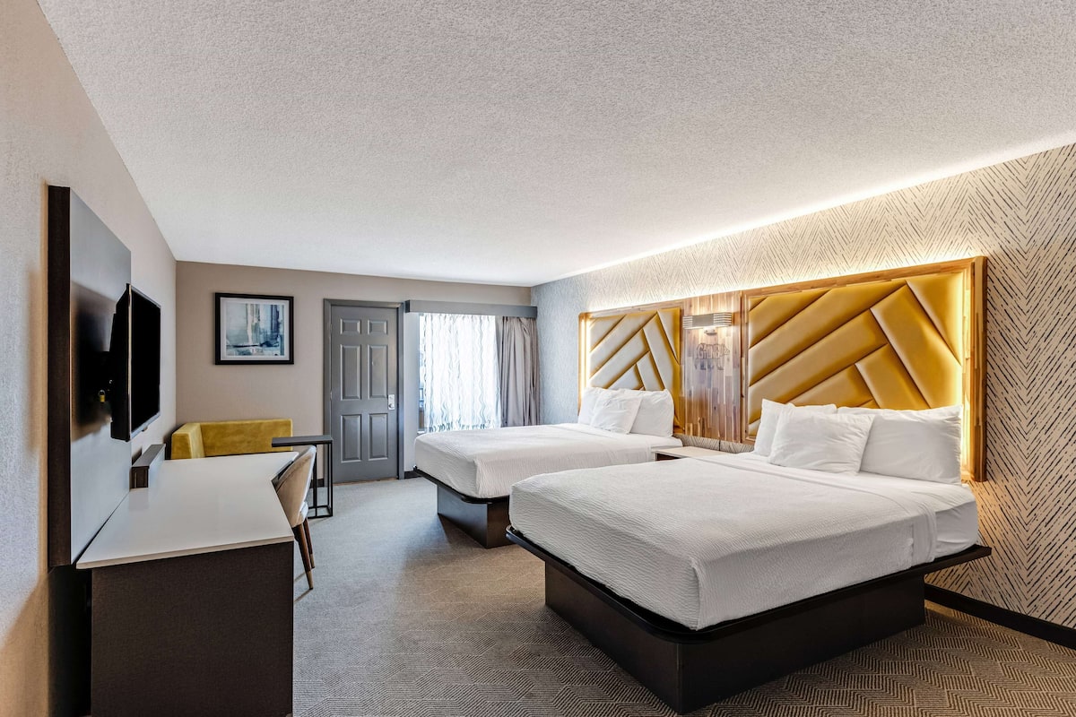 Une chambre d’hôtel avec deux lits, un bureau, une télévision et une grande fenêtre avec des rideaux.