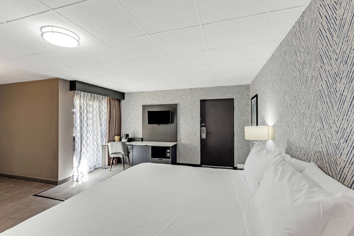 Une chambre d’hôtel avec un grand lit, un bureau avec une chaise, un téléviseur à écran plat et une porte.