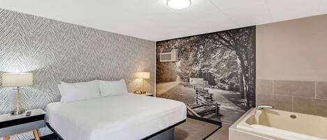 A modern hotel room with a large bed, a separate bathroom with a bathtub, and a mural on the wall.