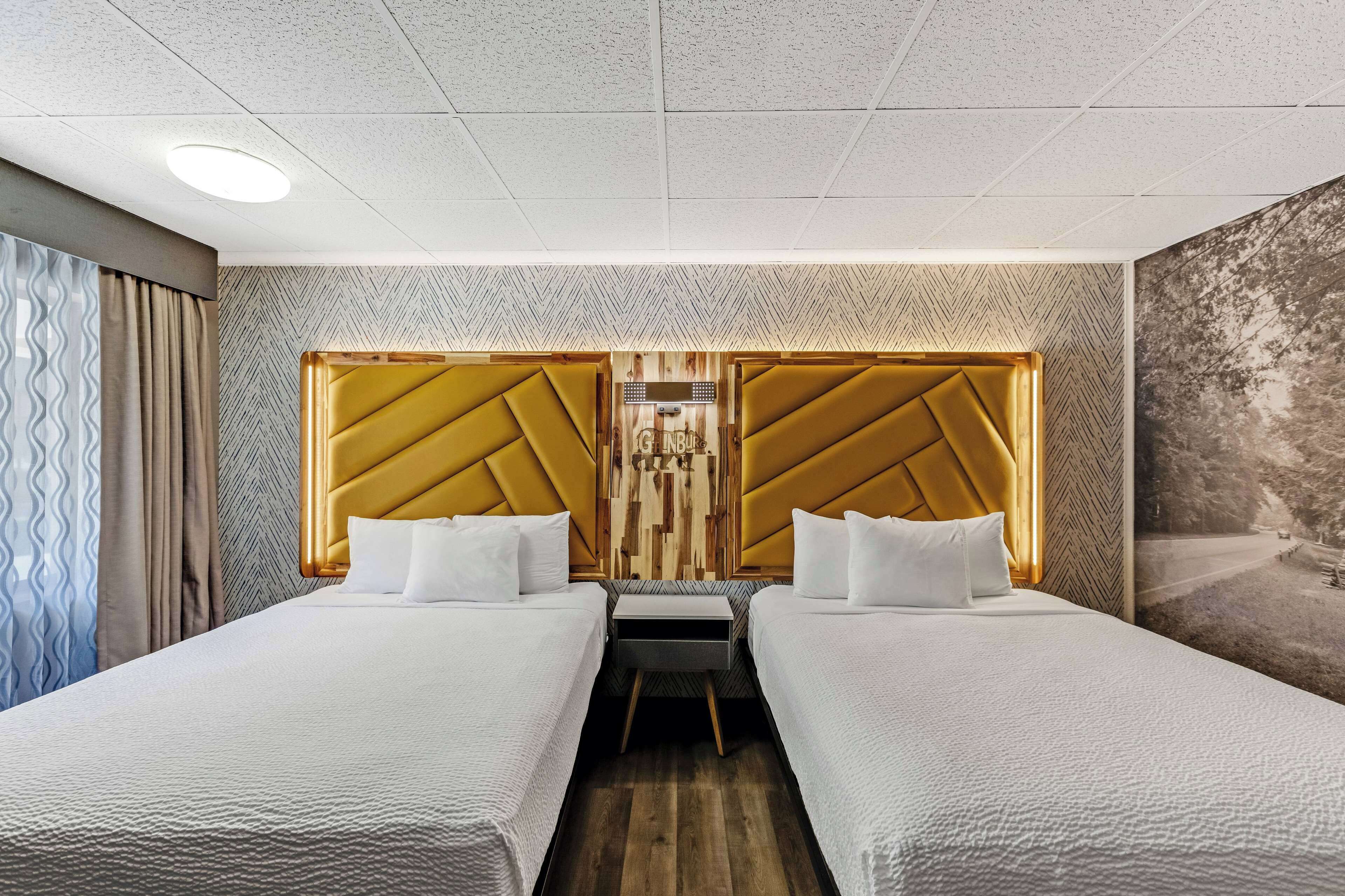 A hotel room with two beds, a wooden headboard, a small table, and a wall-mounted TV.