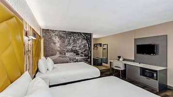 Habitación de hotel con dos camas, un escritorio, televisión y una ventana grande con vistas a árboles.