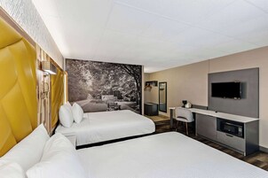 Habitación de hotel con dos camas, un escritorio, televisión y una ventana grande con vistas a árboles.