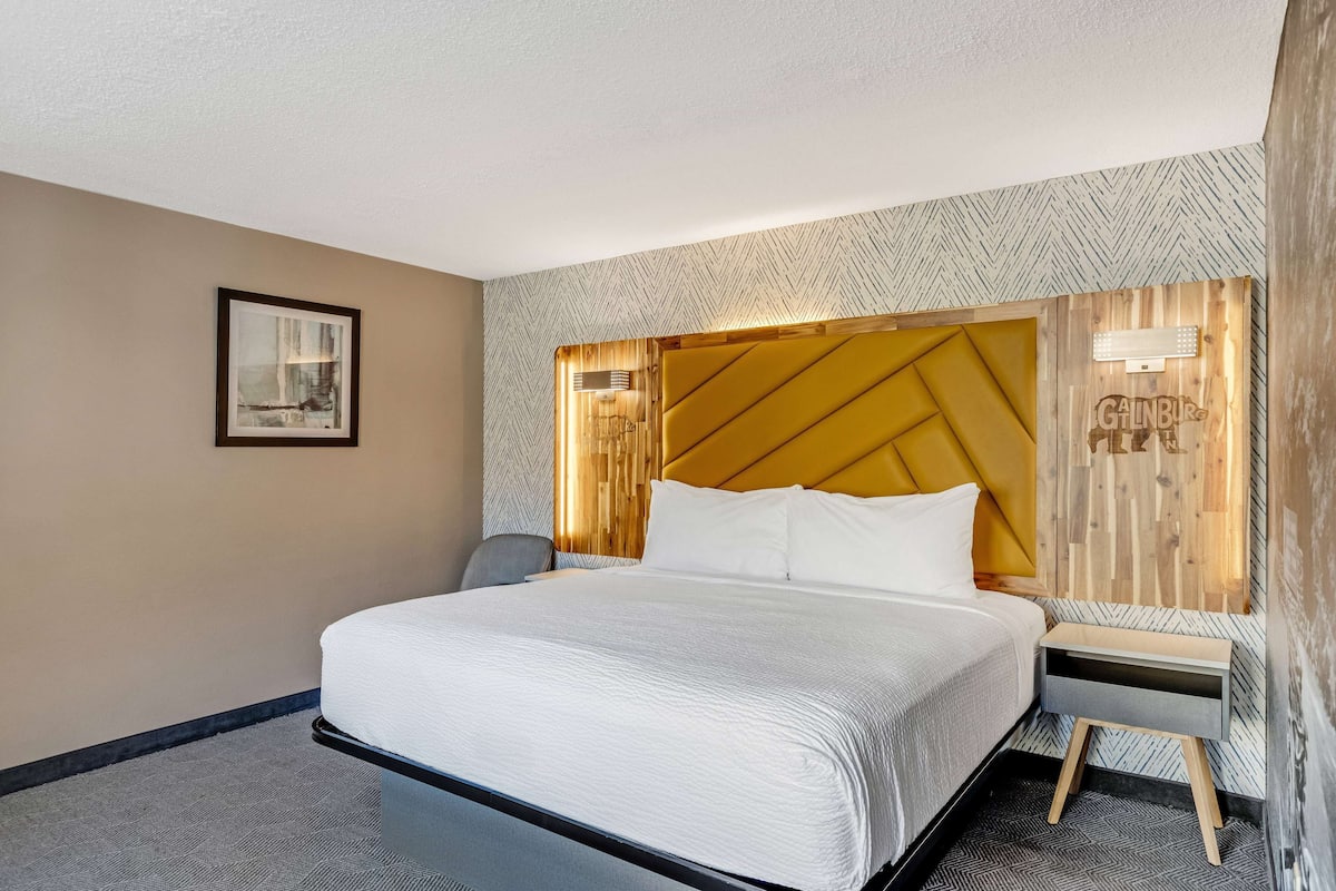 Une chambre d’hôtel avec un grand lit, une table de chevet, une chaise et un luminaire fixé au mur.