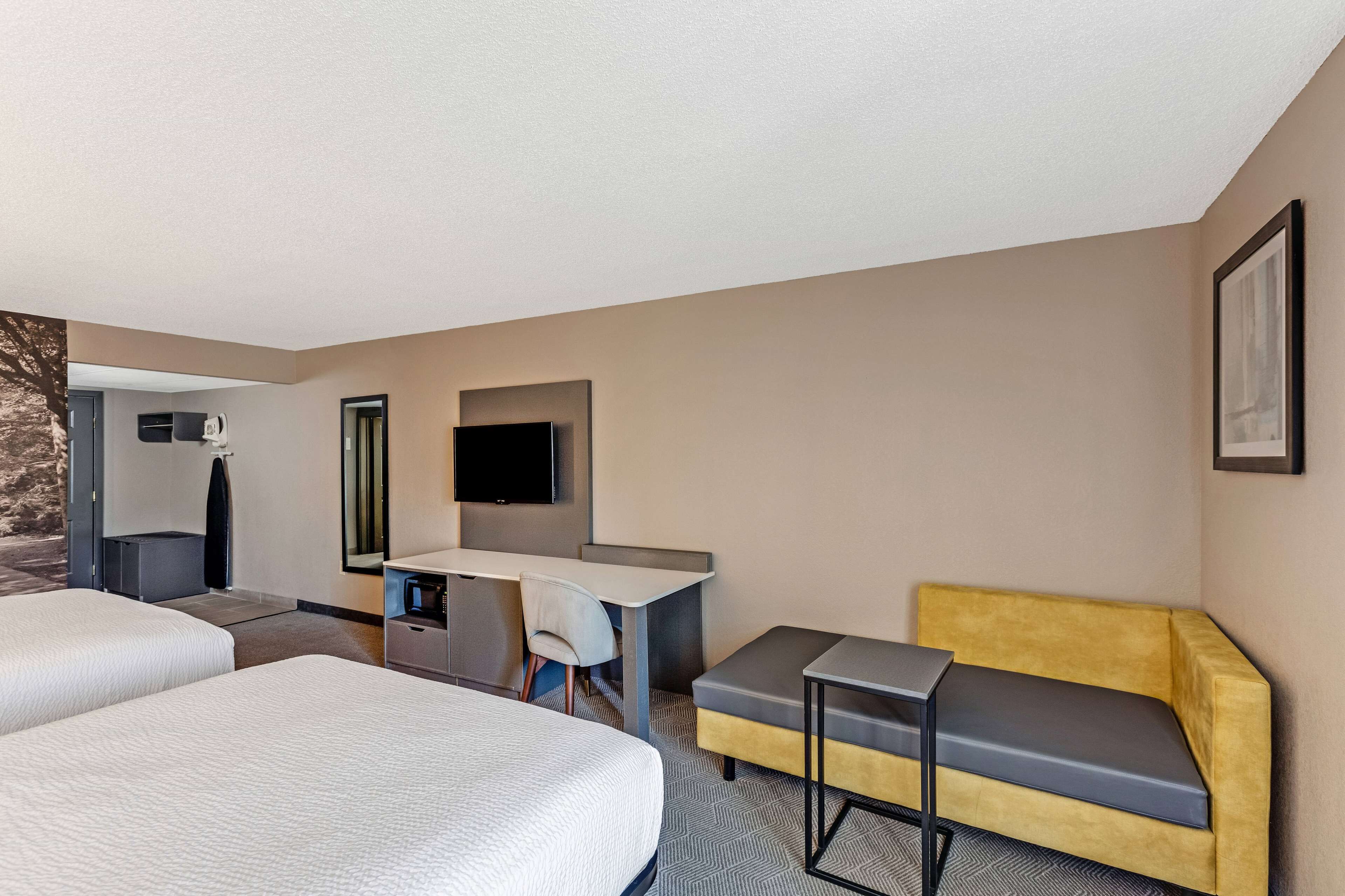 A hotel room with two beds, a desk, a chair, a sofa, a flat-screen TV, and a mirror.