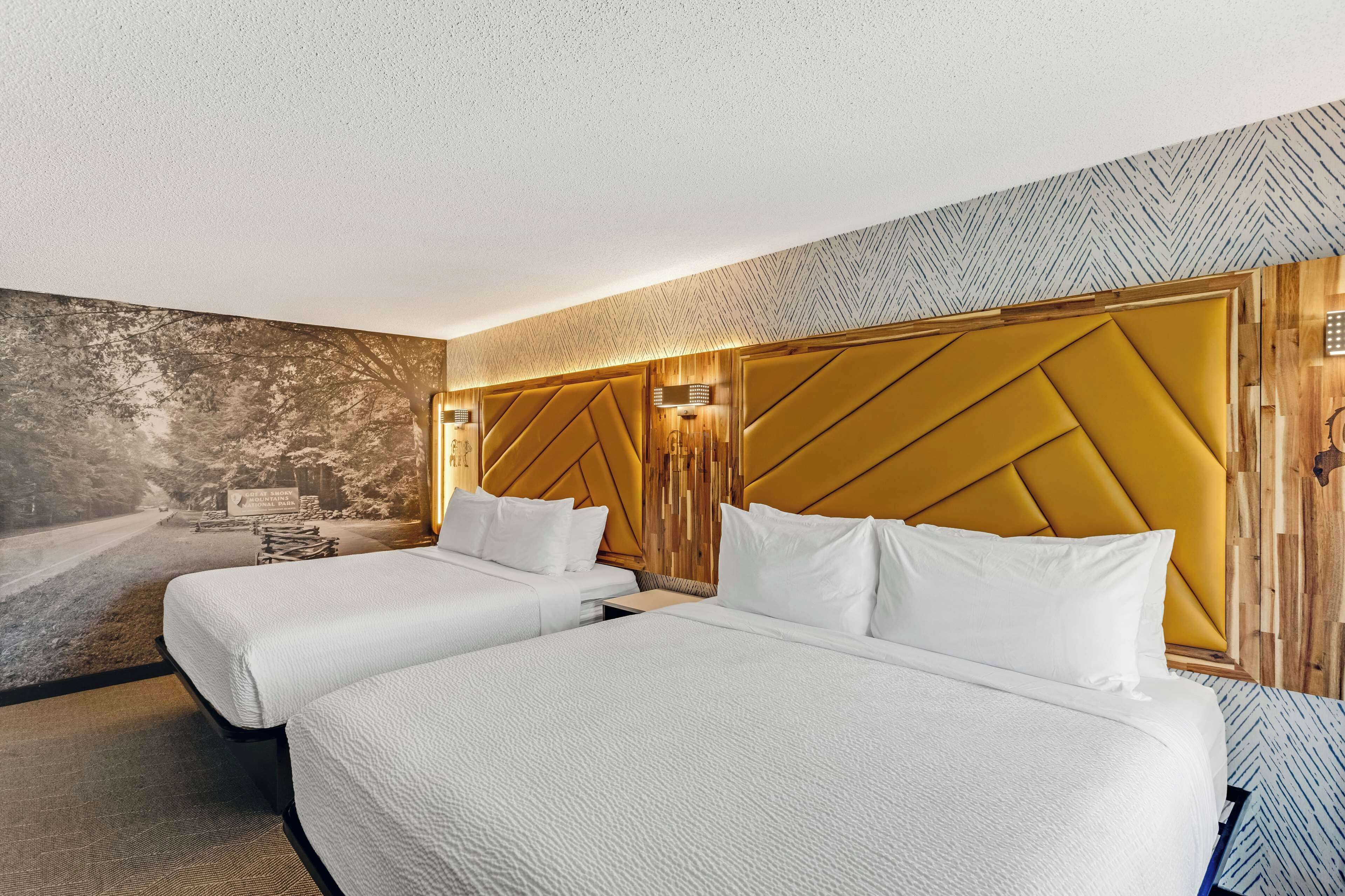 A hotel room with two beds, a large mural, and a wooden headboard.
