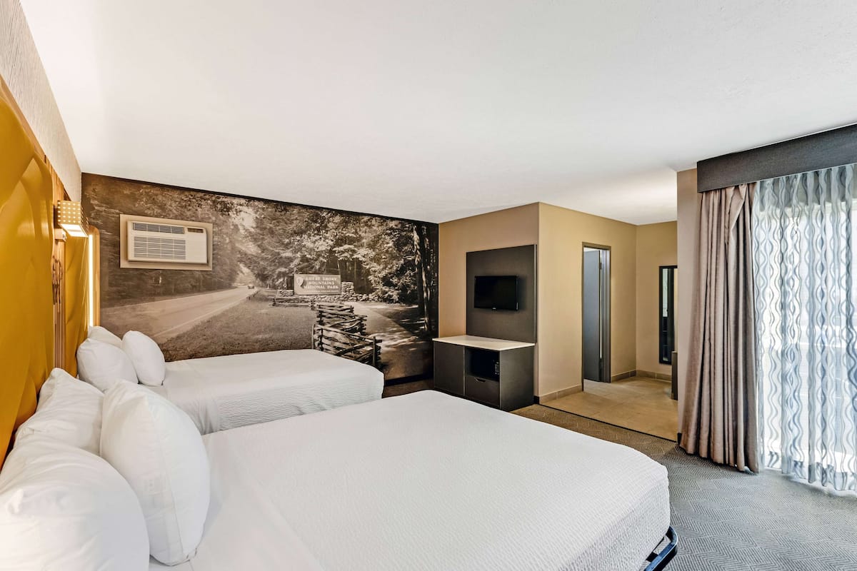 Une chambre d’hôtel avec deux lits, un téléviseur à écran plat, un petit bureau et une grande fenêtre avec des rideaux.