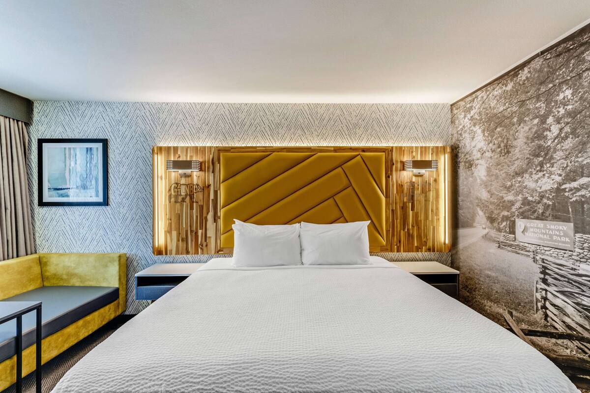 Une chambre d’hôtel avec un grand lit, un canapé jaune, un tableau encadré au mur et une affiche du parc national des Great Smoky Mountains.