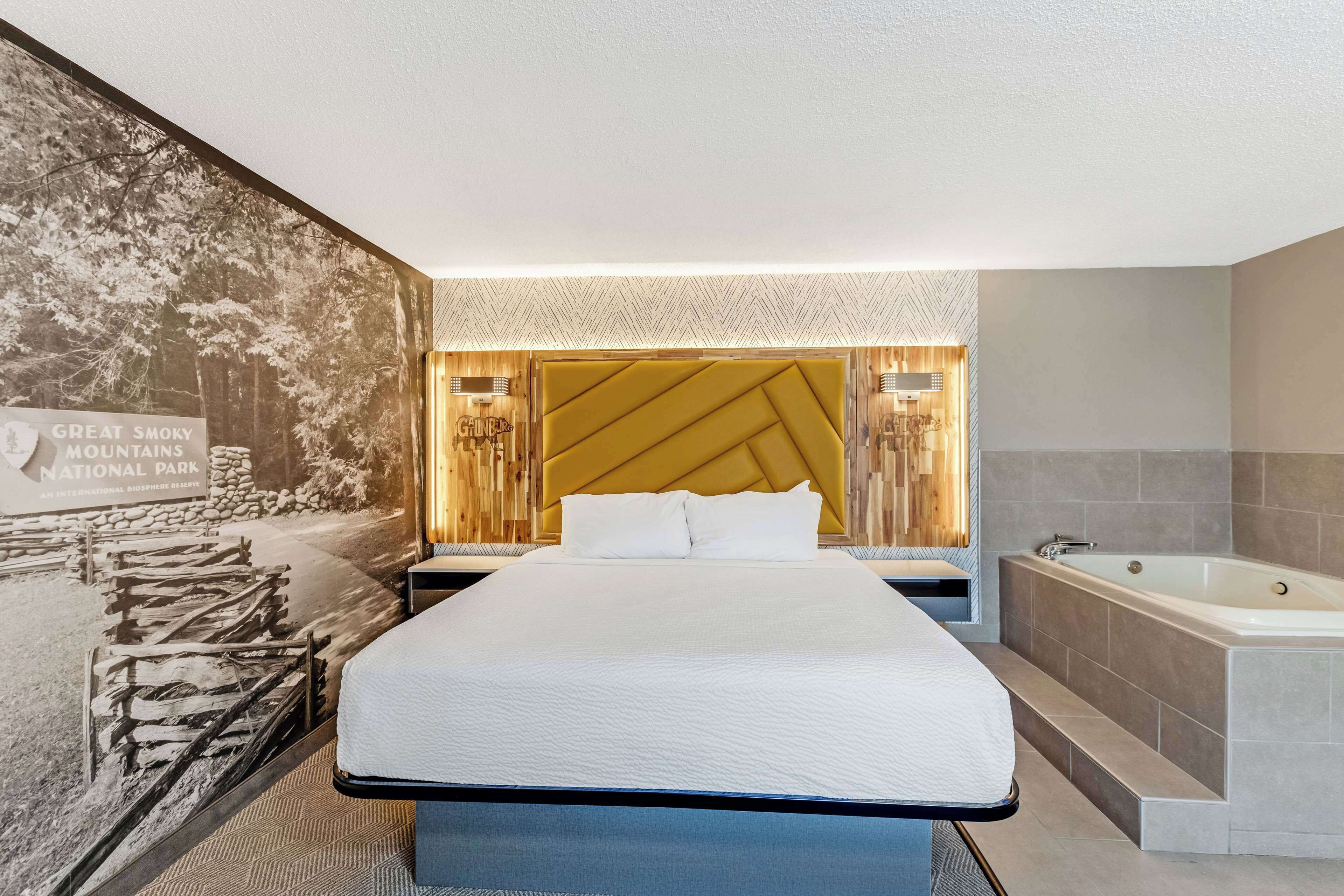 Quarto de hotel moderno com uma cama grande, banheira integrada e um mural na parede.