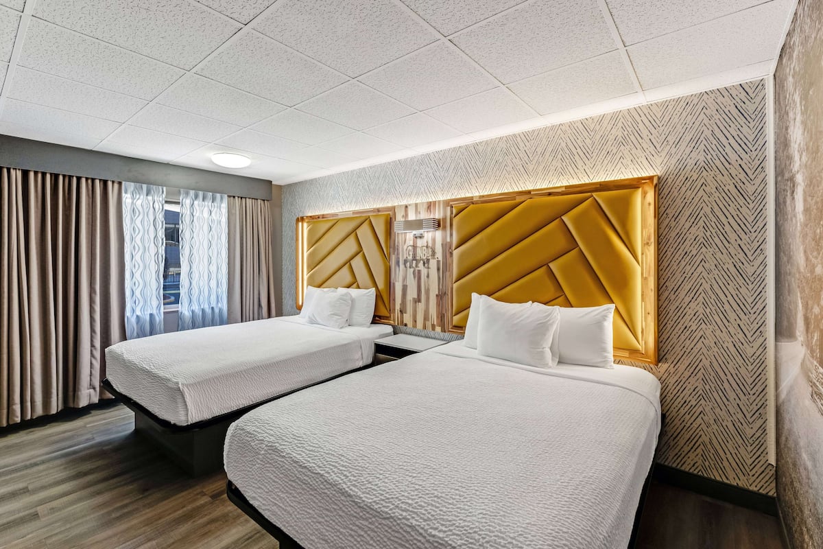 Une chambre d’hôtel avec deux lits, une tête de lit en bois, un mur à motifs et une fenêtre avec des rideaux.