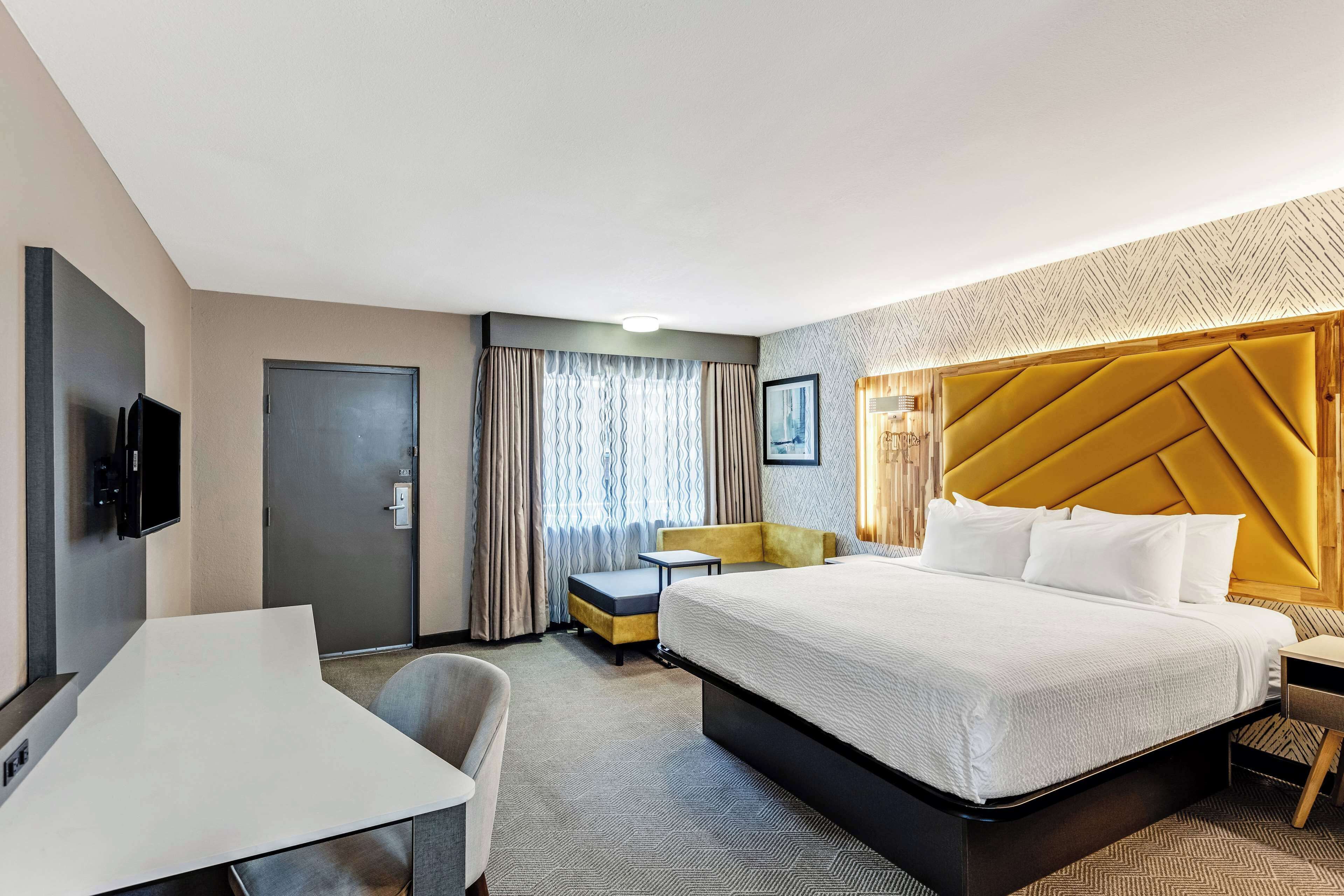 A hotel room with a large bed, a desk, a chair, a TV, and a window with curtains.