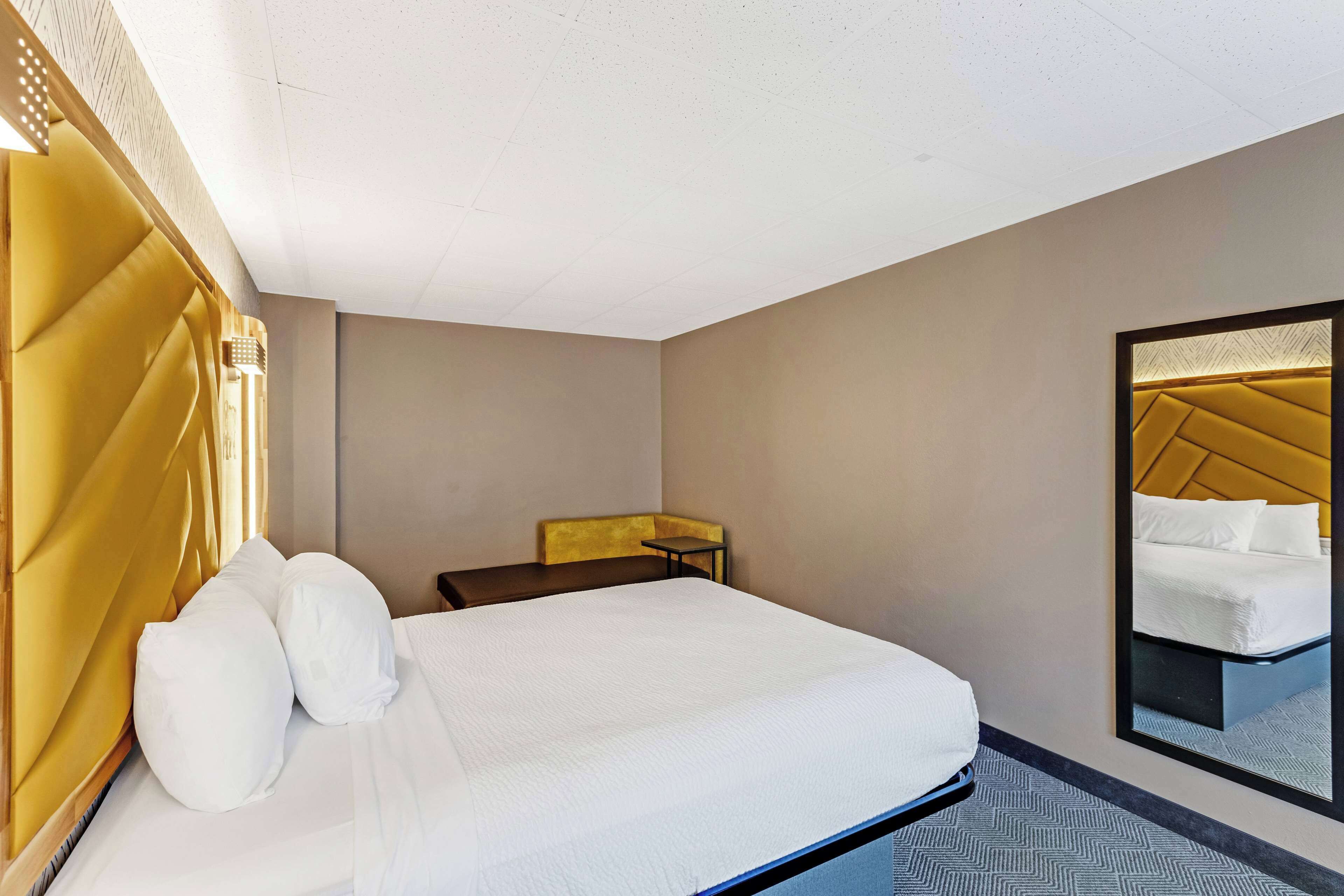 A hotel room with a large bed, a bedside table, a mirror, and a headboard with a unique design.