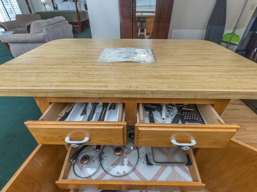 A wooden desk with two drawers containing kitchen utensils and a packet of napkins.