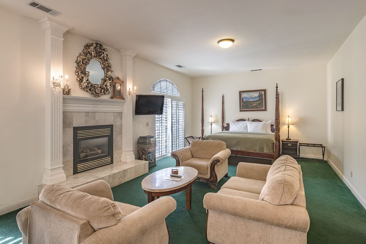 A hotel room with a fireplace, a bed, a television, and a view of the outdoors.