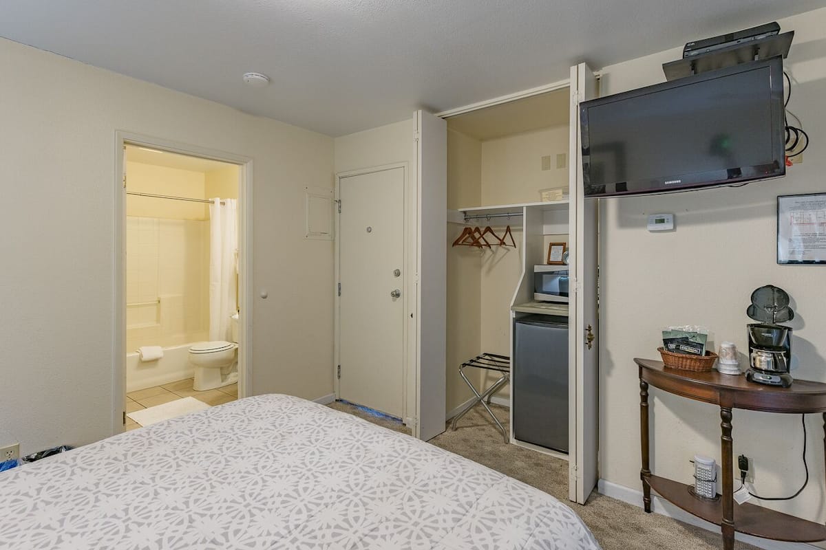 A hotel room with a bed, a television, a desk with a coffee maker, and a walk-in closet.