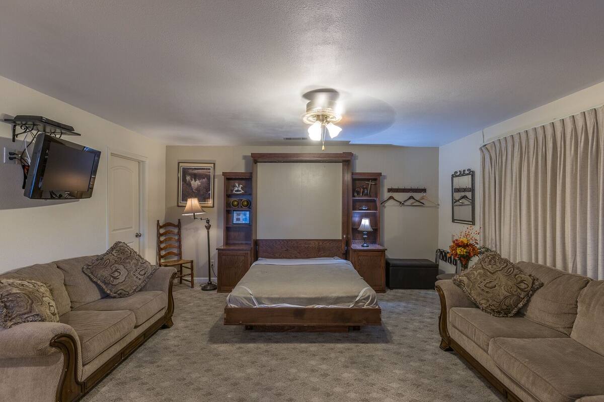 A bedroom with a bed, two sofas, a TV, a ceiling fan, and a mirror.