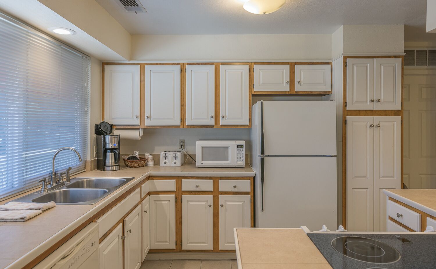 A compact kitchen with white cabinets, a built-in microwave, a refrigerator, and a sink.