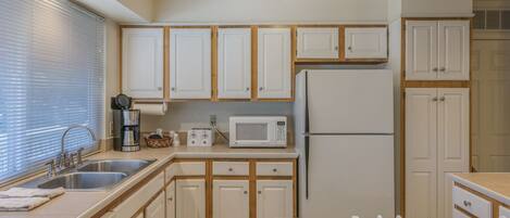 A compact kitchen with white cabinets, a built-in microwave, a refrigerator, and a sink.