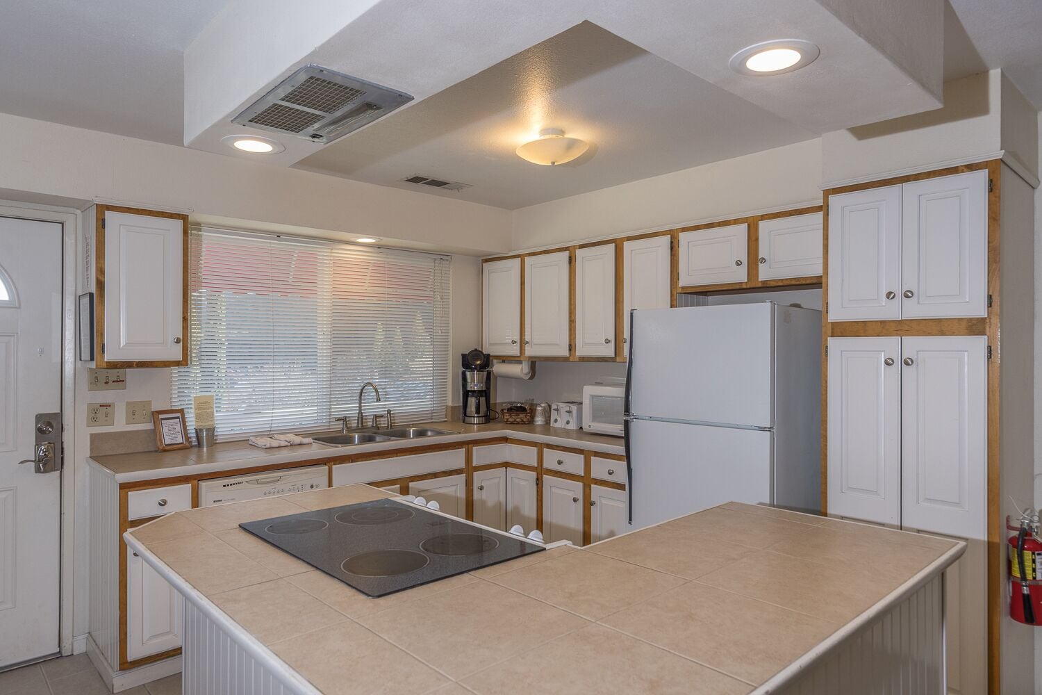 A kitchen with white cabinets, a central island with a stovetop, a refrigerator, and a microwave.