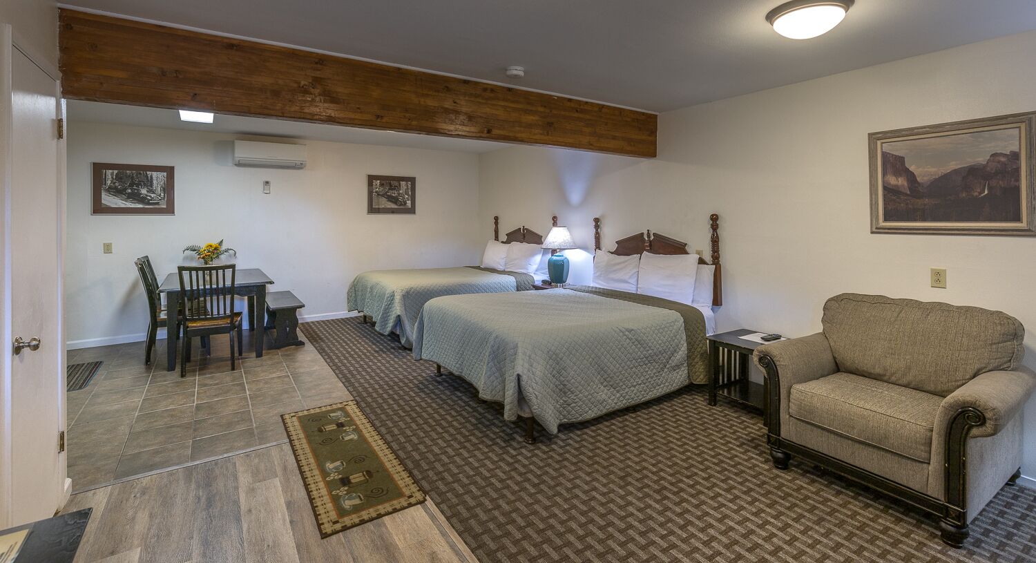 Ein Zimmer mit zwei Betten, einem Esstisch mit Stühlen, einem Sofa und einem Bild an der Wand.
