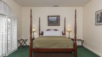 A four-poster bed with a quilted bedspread, two bedside lamps, and a framed landscape painting above the bed.