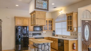 A kitchen with wooden cabinets, a black refrigerator, a microwave, a stove, and a stone island with stools. - 5th Street Inn (Mariposa)