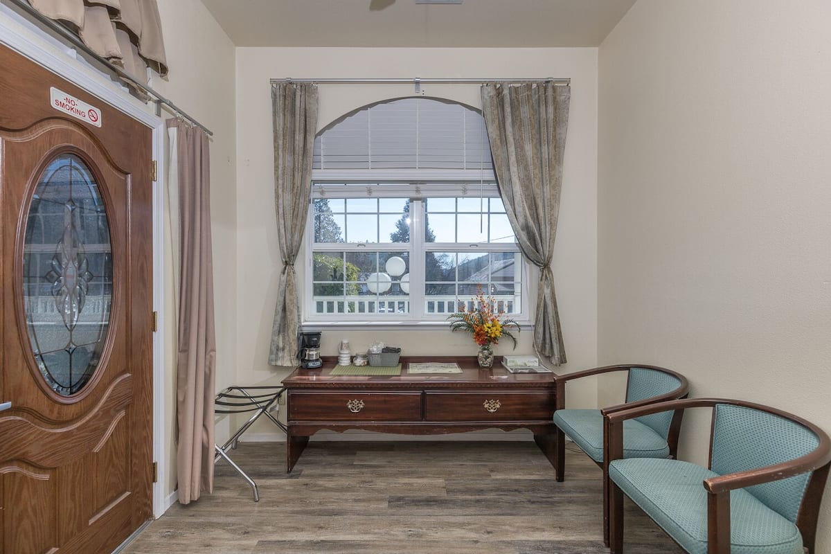 A room with a wooden desk, a chair, a window with curtains, and a door with a sign.