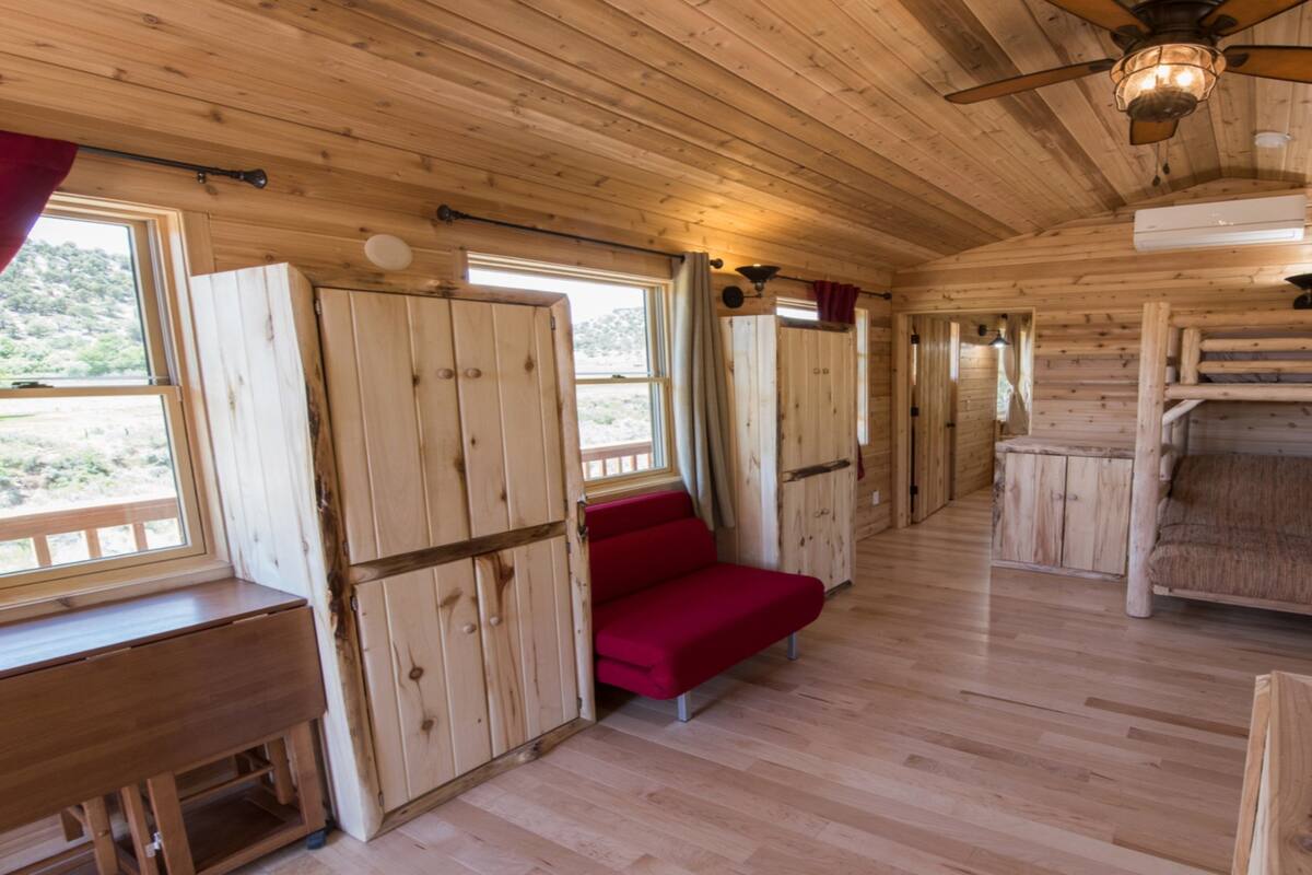 A cabin interior with wooden walls, a bunk bed, a red sofa, and a desk.