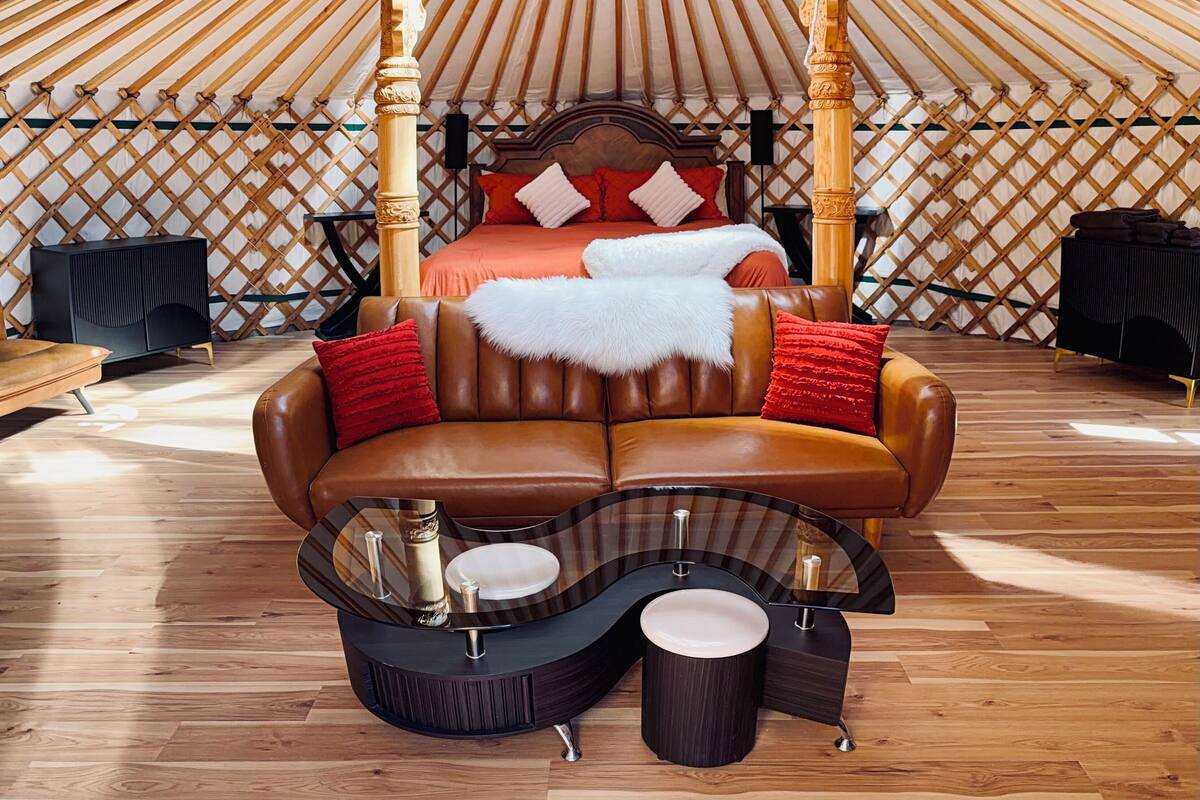 A luxurious room with a central bed, a leather sofa, and a unique ceiling design.